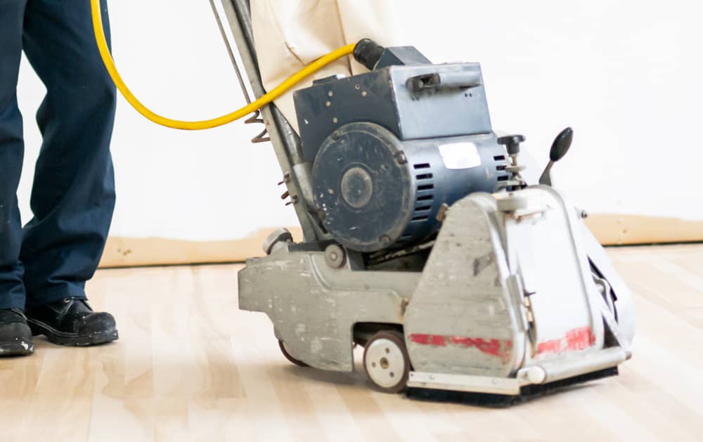 Das Bild zeigt einen Ausschnitt einer Bodenschleifmaschine auf einem Holzboden.